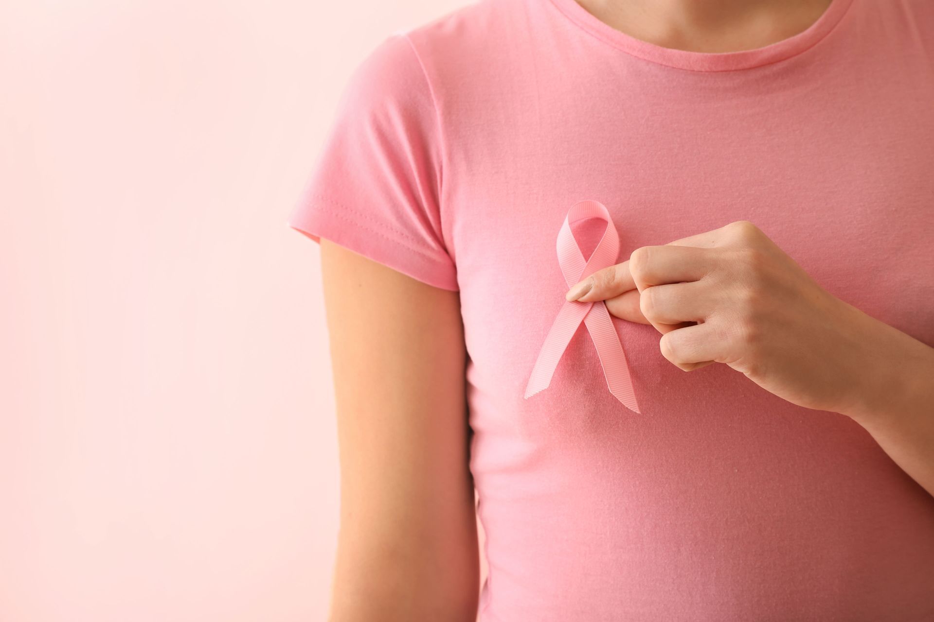 Pessoa vestindo uma camisa rosa prendendo uma fita rosa de conscientização sobre o câncer de mama no peito.