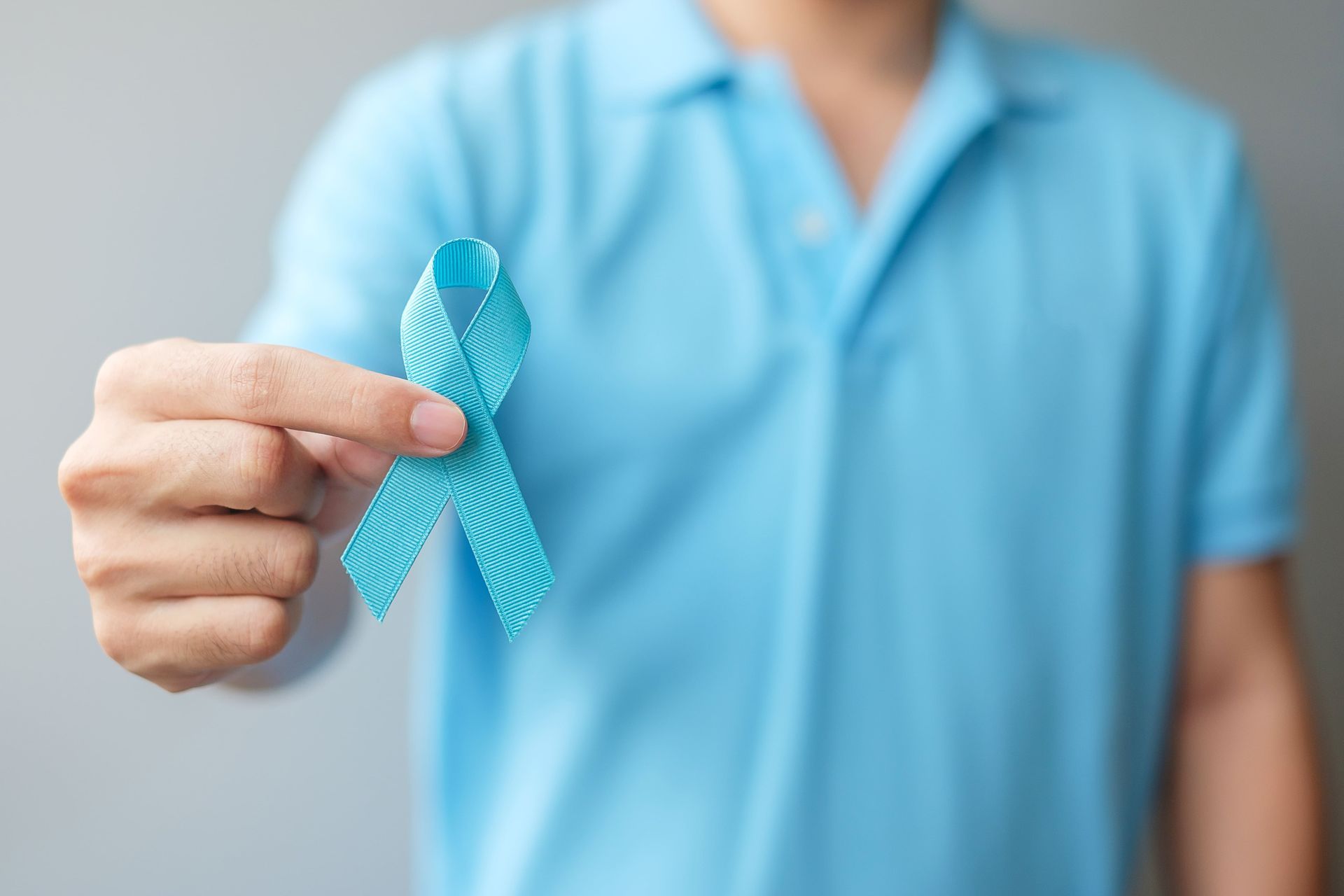 Pessoa segurando uma fita azul de conscientização contra um fundo claro.