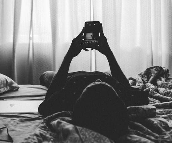 A woman is laying on a bed taking a picture with her phone.
