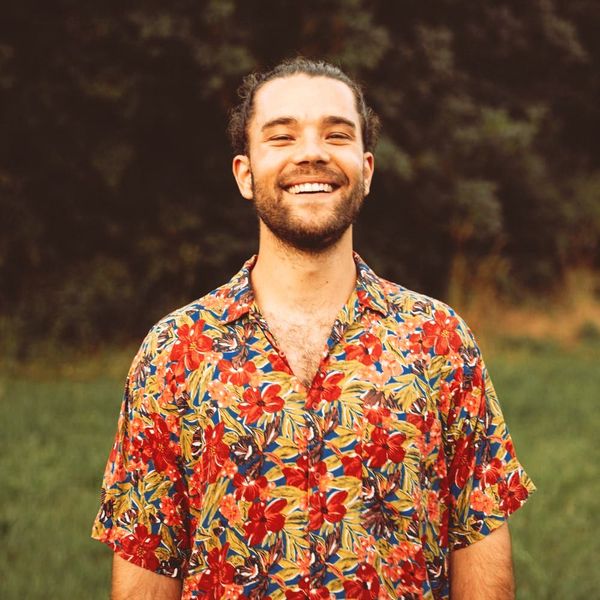 A man with a beard wearing a colorful floral shirt is smiling in a field.