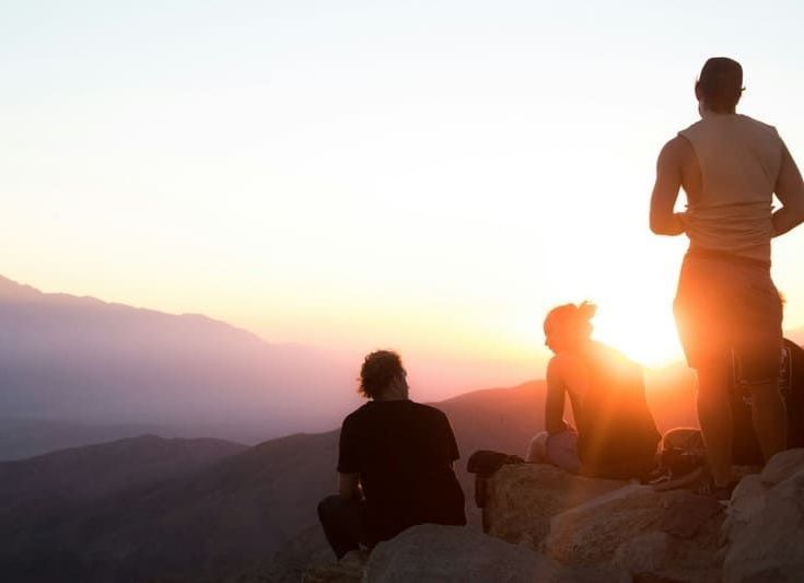 A group of people are sitting on top of a mountain at sunset.