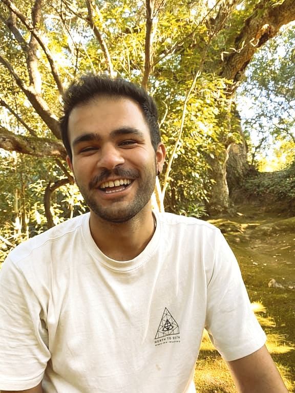 A man in a white shirt is smiling in front of a tree.