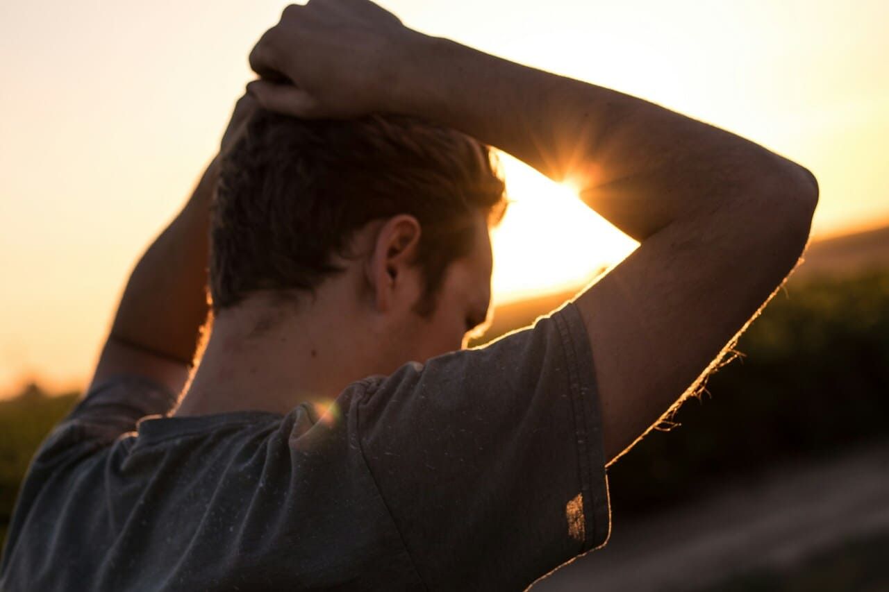 A man is looking at the sun while holding his head.