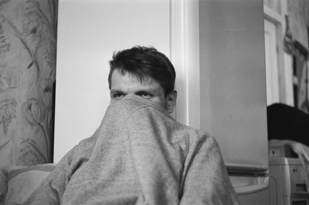 A black and white photo of a man covering his face with a blanket.