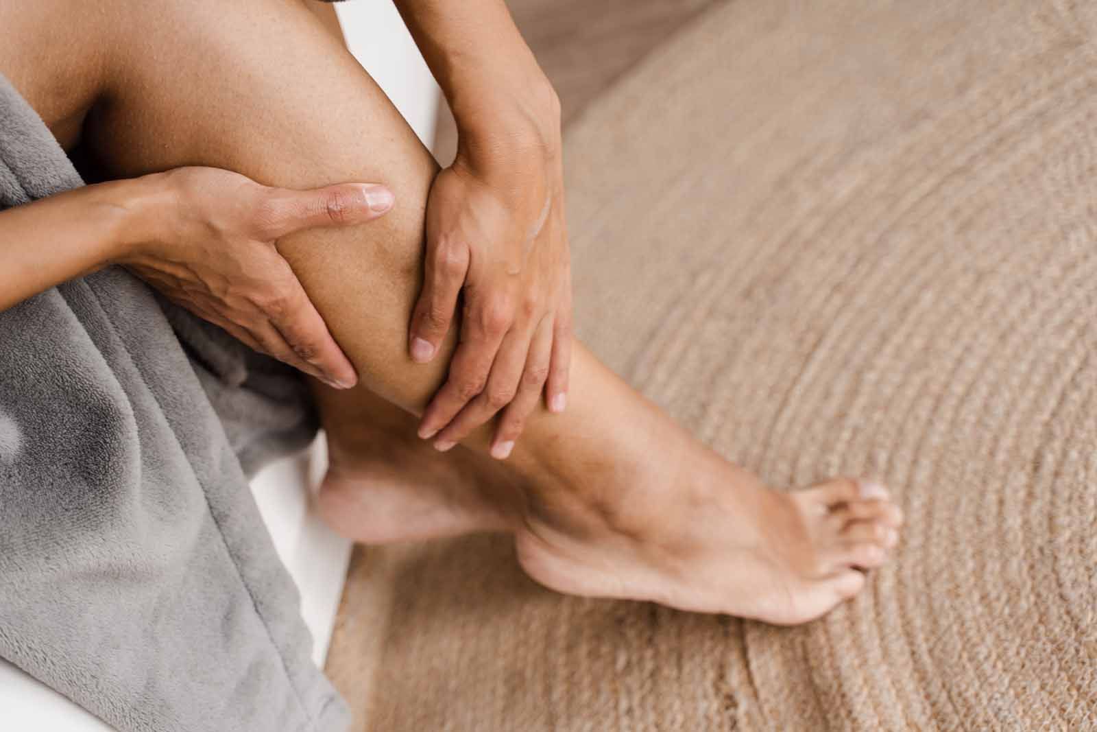 A woman is sitting on a bed with a towel wrapped around her legs.