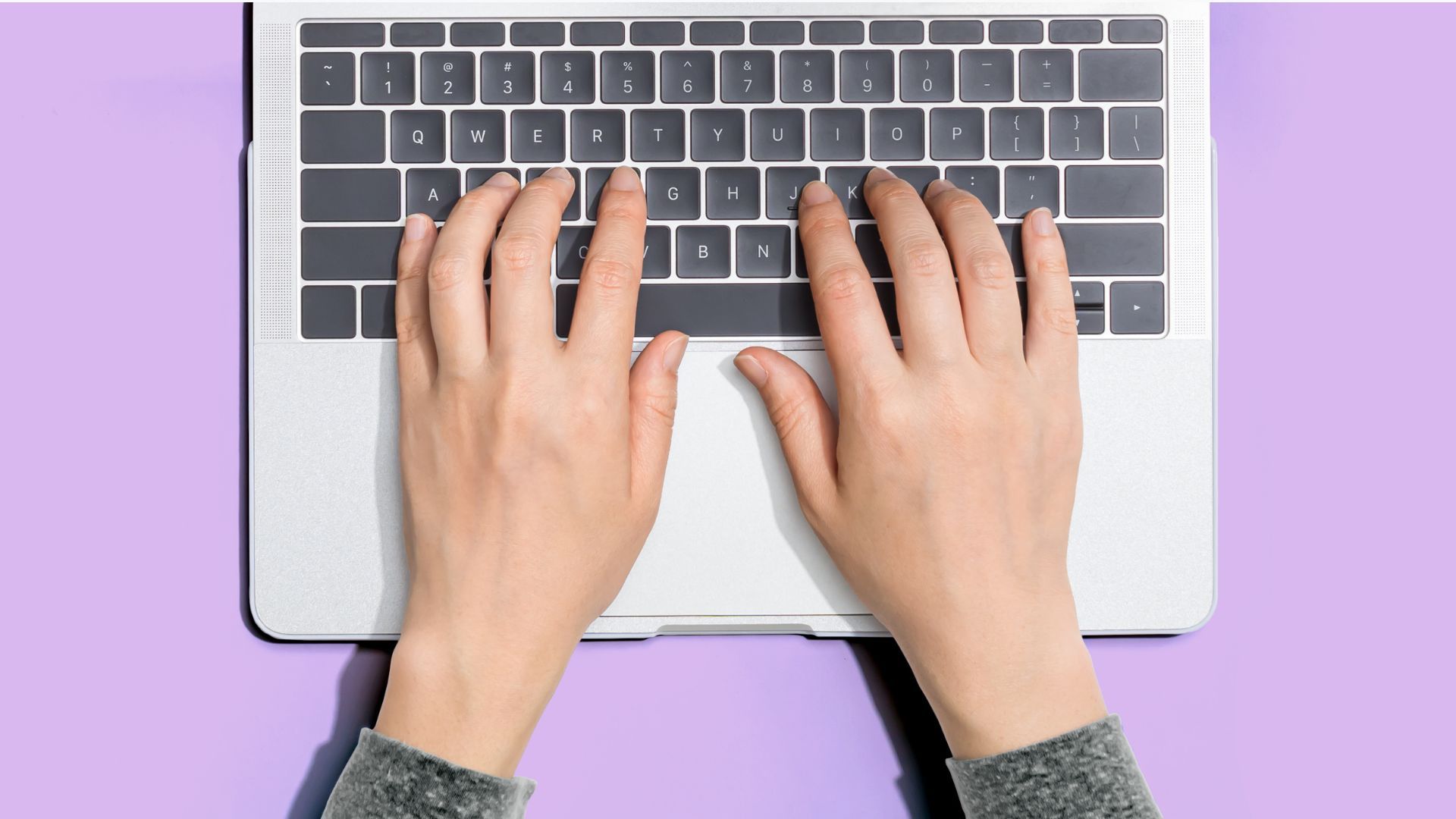 A person is typing on a laptop computer on a purple background.