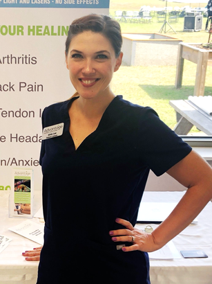 A professional stands in dark blue scrubs with a hand on her hip in front of a medical information booth.