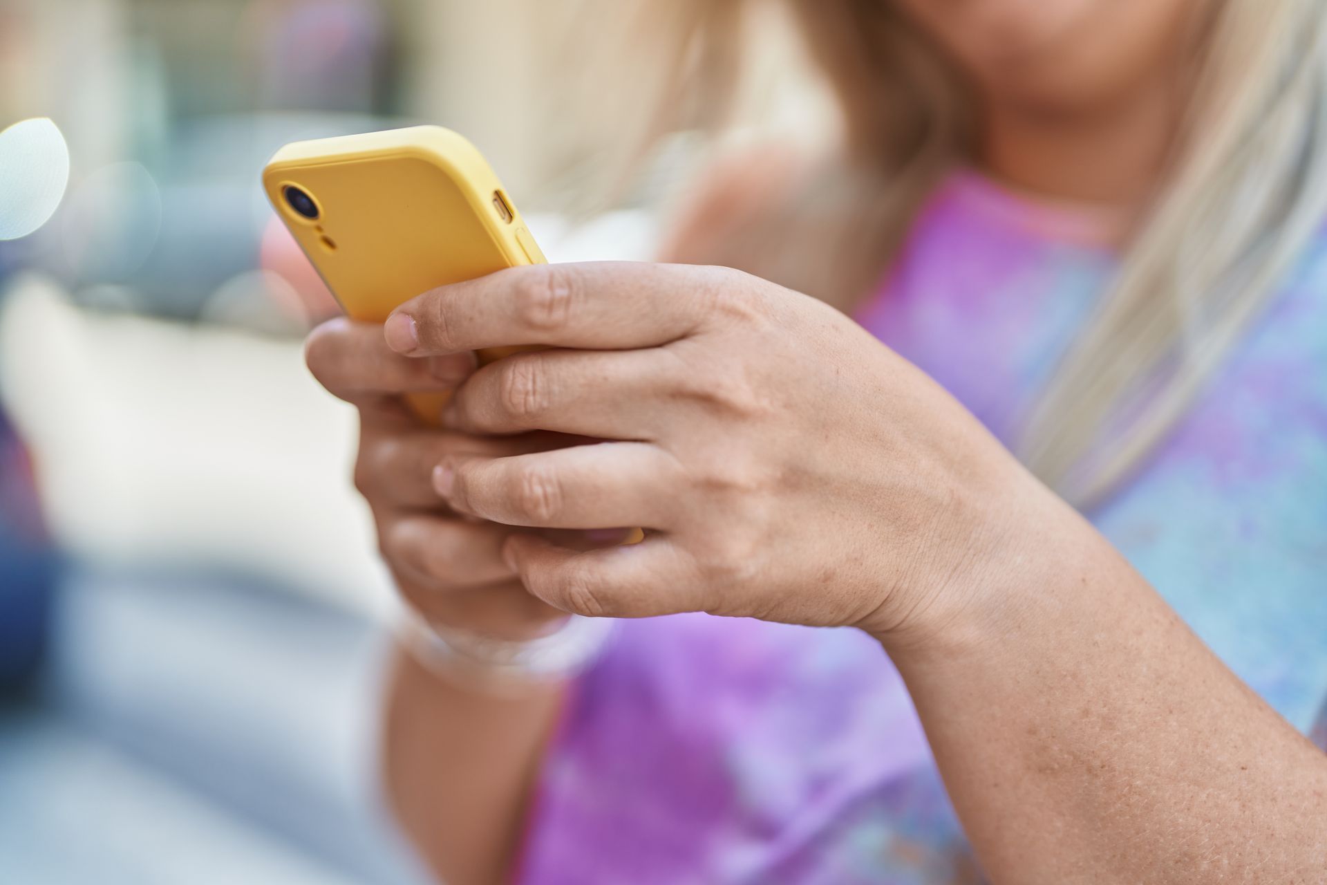 A woman is holding a yellow cell phone in her hands.