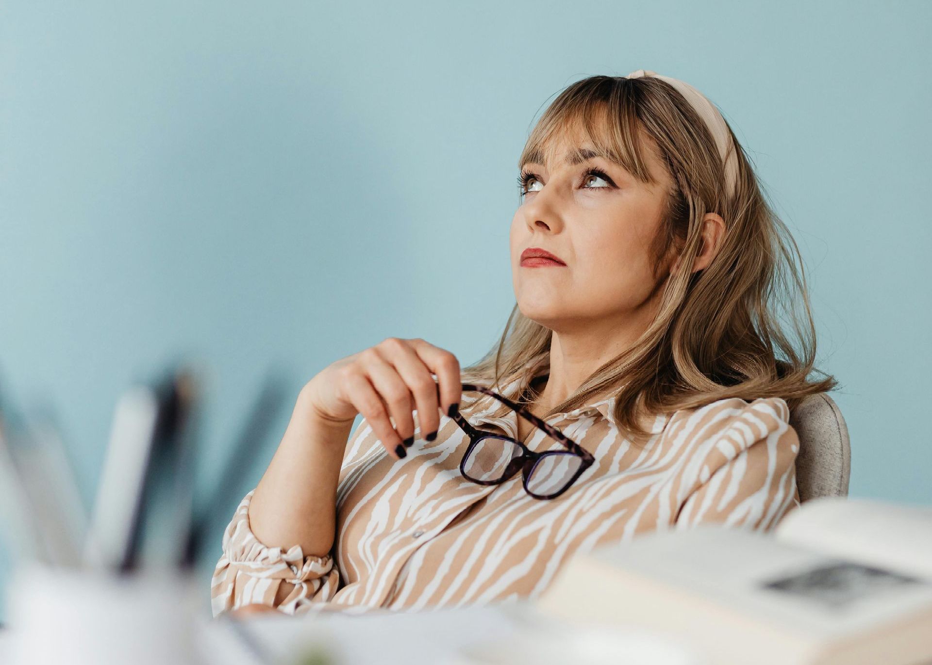 A woman is sitting at a desk wearing glasses and looking up.