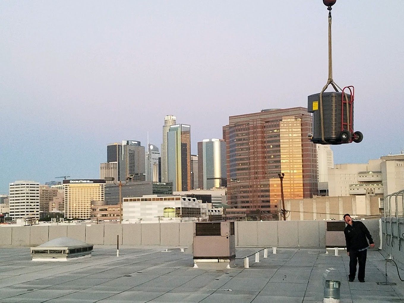 A man is standing on a rooftop looking at a crane lifting a large box