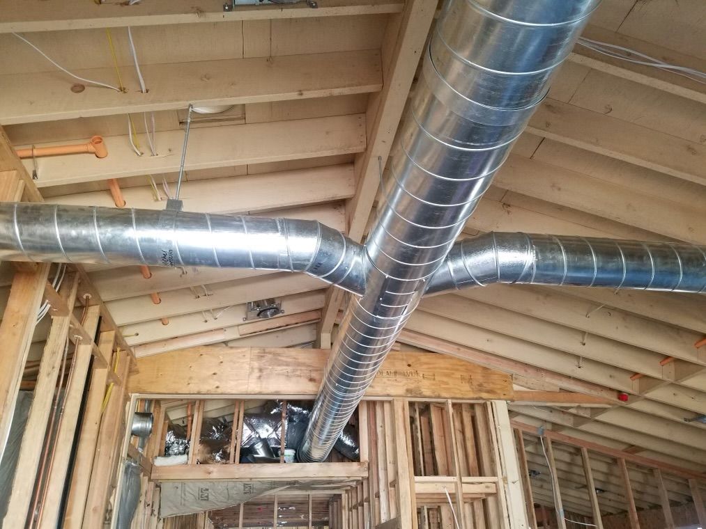 A large metal pipe is hanging from the ceiling of a house under construction.