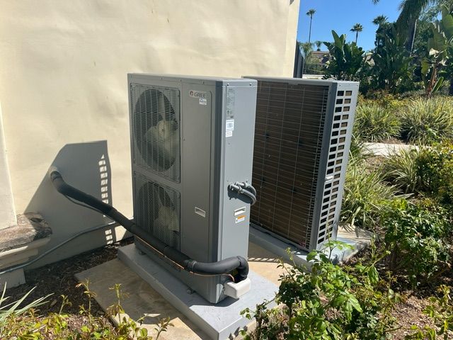 Two men are working on an air conditioner on the roof of a building.