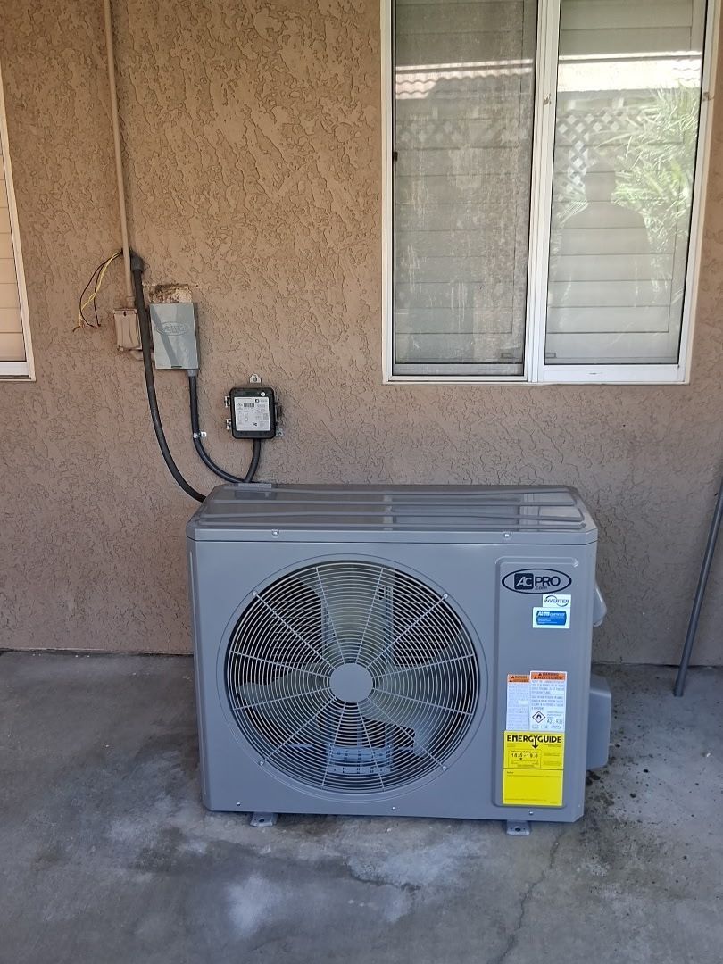 Outdoor air conditioner unit beside a stucco wall and window, with electrical conduit and outlet nearby.