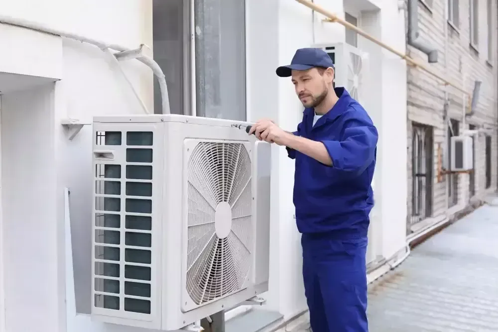 Technician in blue uniform inspecting large silver HVAC ductwork in a ceiling space