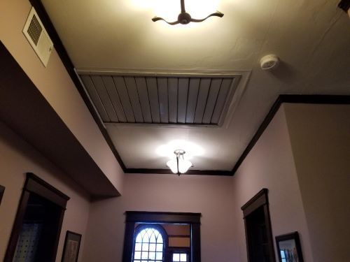 Wooden attic with a large silver fan mounted on a wall and a blue device on the left.