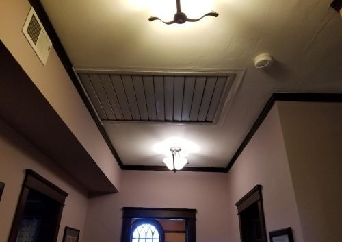 Indoor hallway ceiling with two lights, vents, and a front door below.