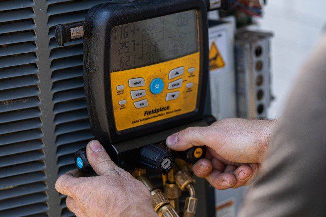 Hands adjusting a yellow HVAC control panel with brass valves and black hoses
