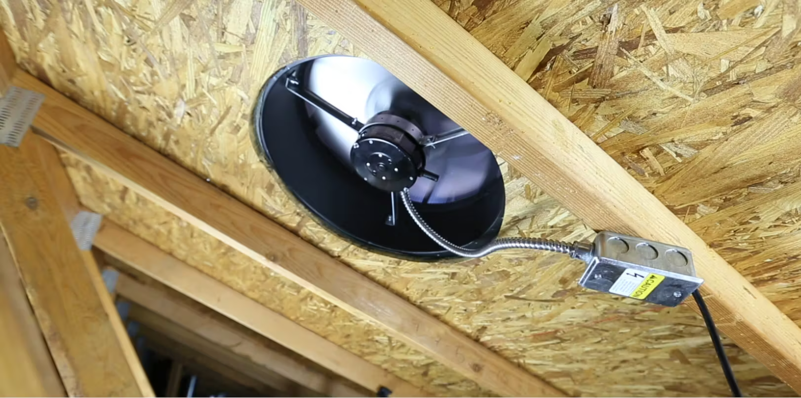 Black dome light fixture mounted on an OSB ceiling with exposed wiring and a yellow connector