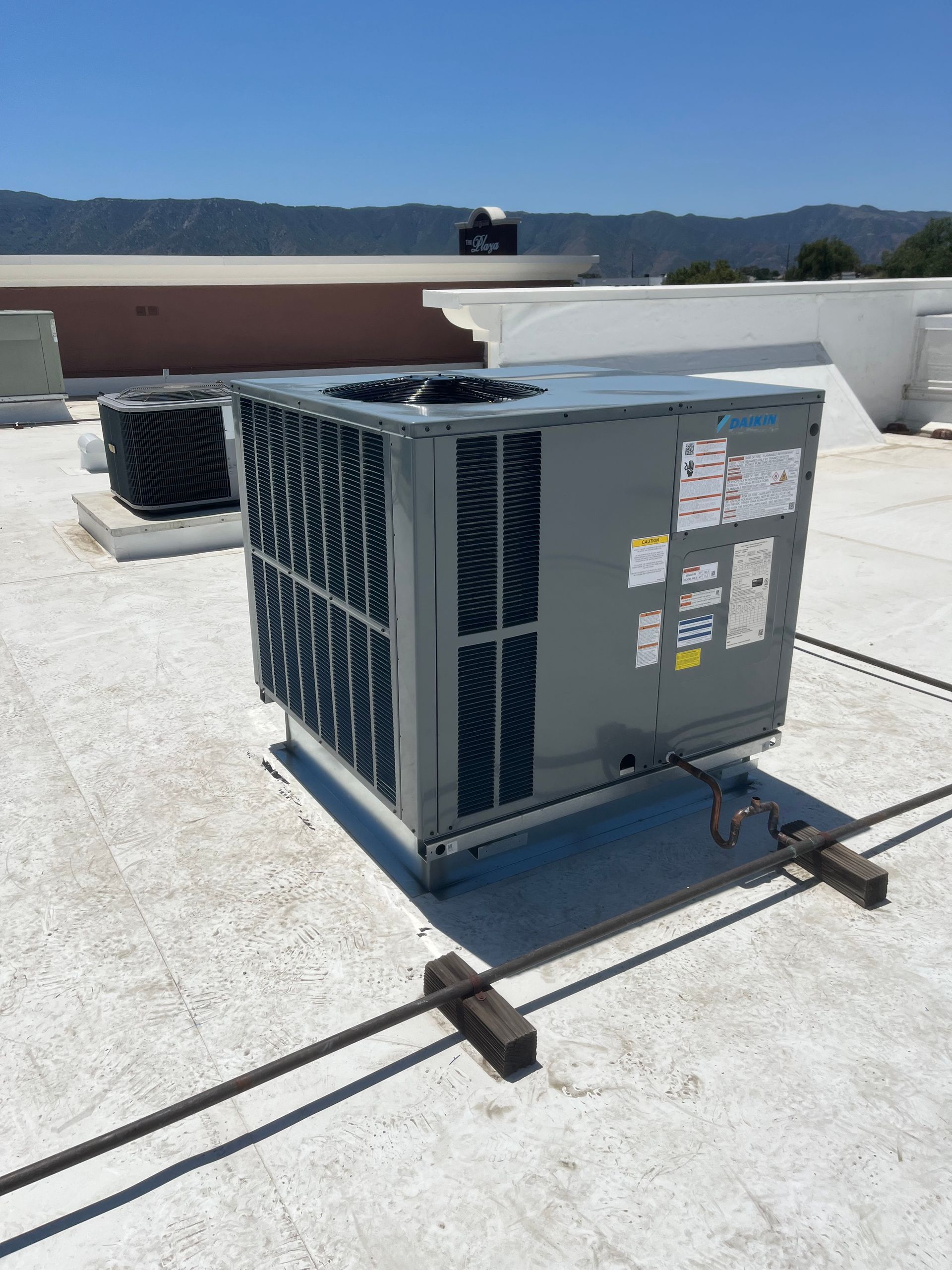 Outdoor rooftop HVAC unit with metal ducting on a white flat roof under a clear sky
