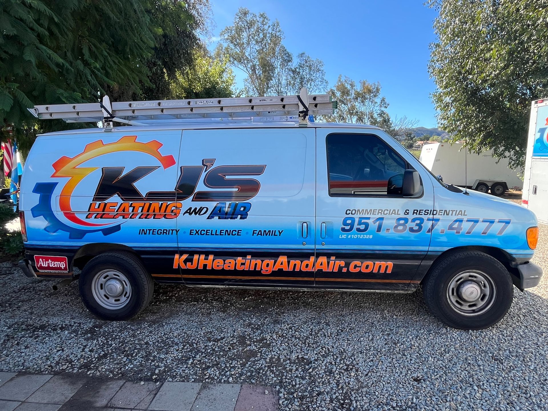 K&N Heating and Air service van parked outdoors, white and orange with company branding and phone number.