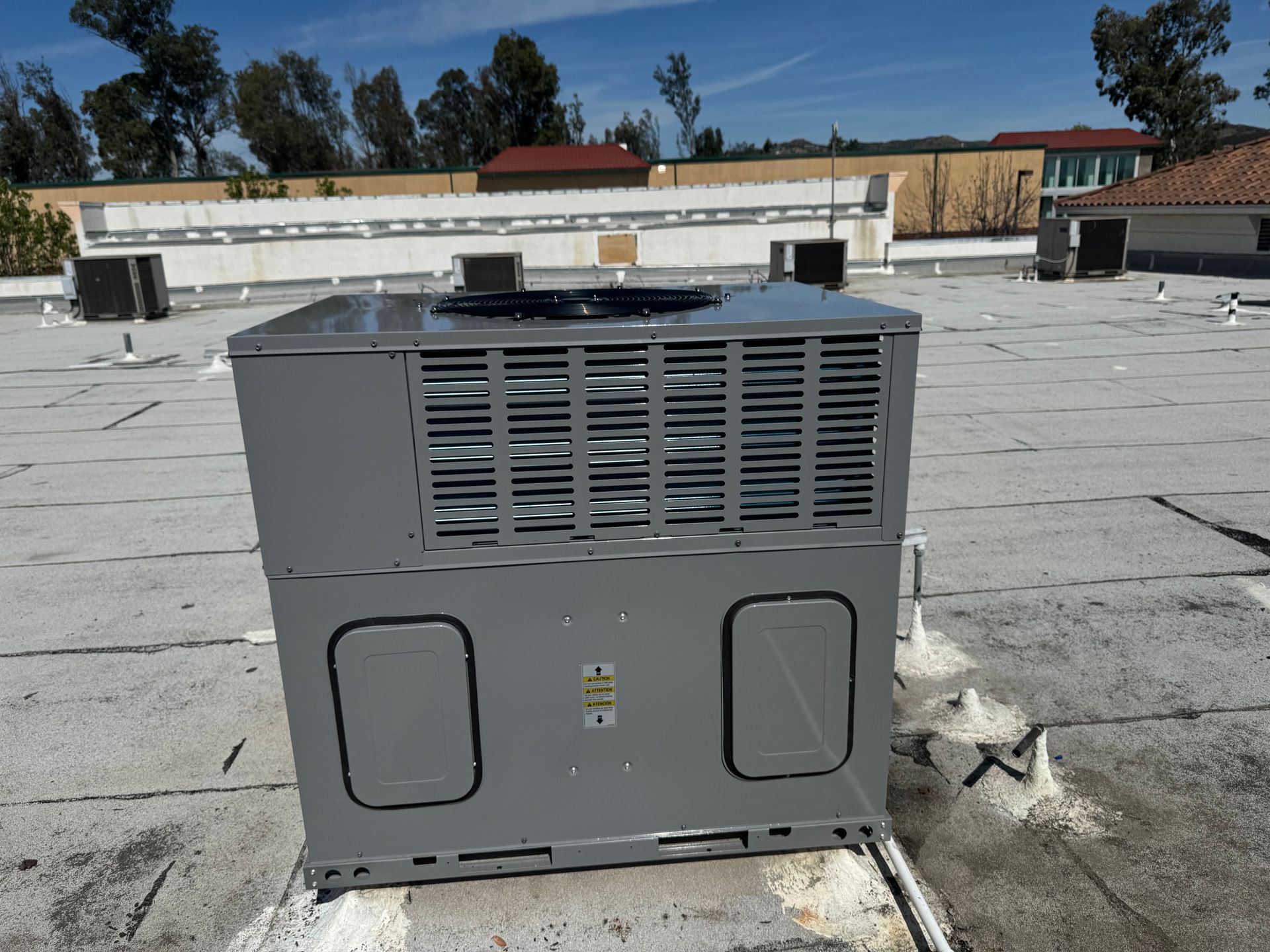 Gray rooftop HVAC unit on a flat roof under a clear blue sky with trees and buildings in the background