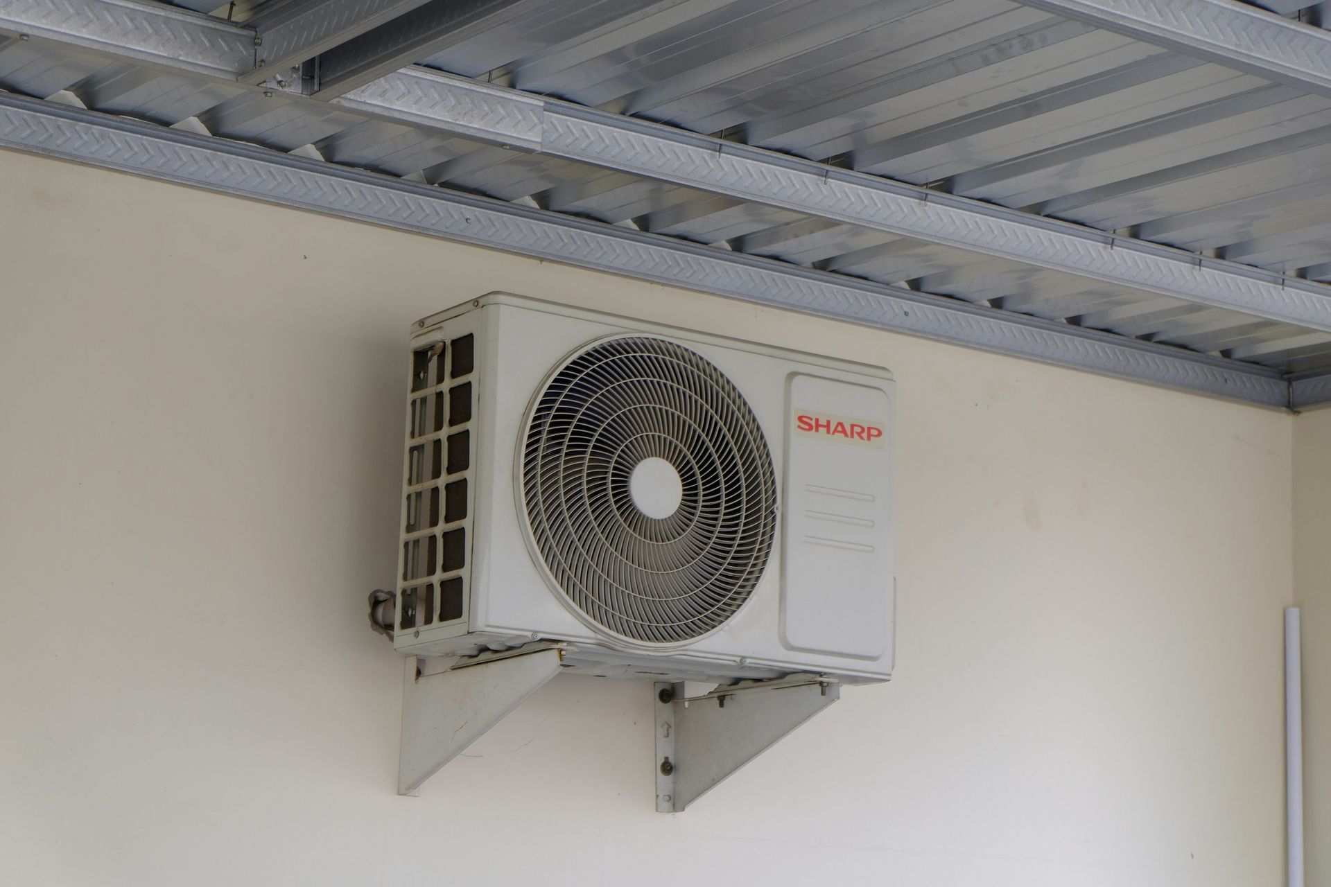 Wall-mounted air conditioner unit with a large fan in an industrial room, under a corrugated metal ceiling