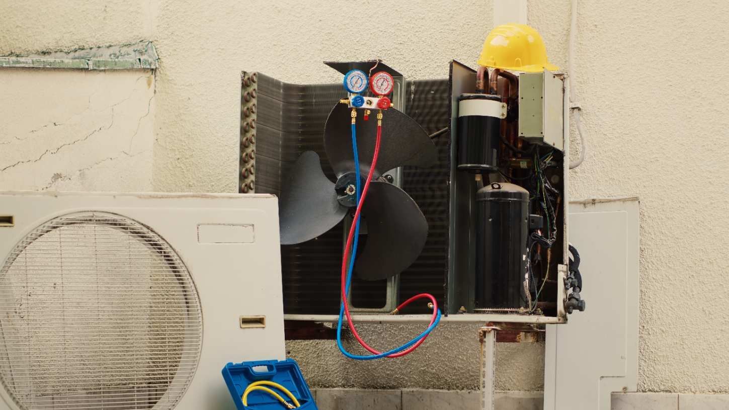 Technician inspecting an outdoor air conditioner unit beside a house with a wrench and gauges