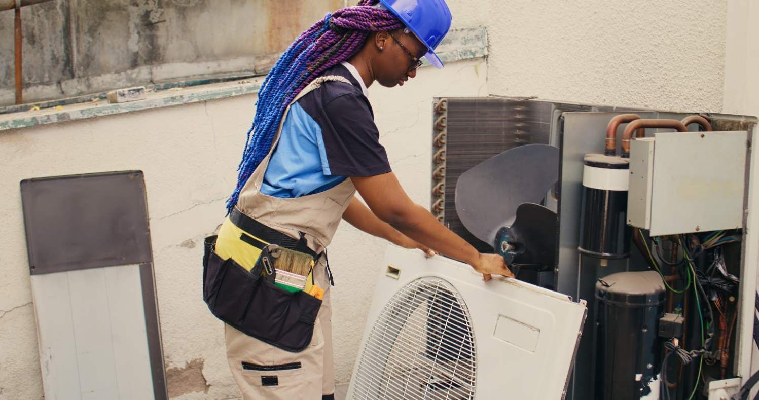 Technician servicing outdoor air conditioner unit with tools beside a house