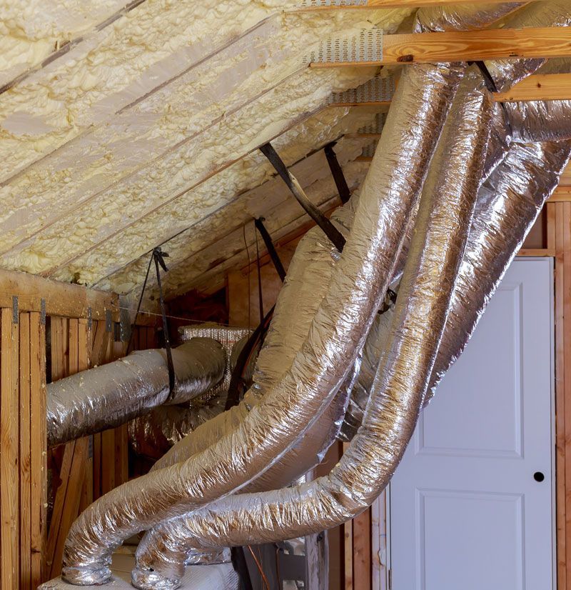Attic with insulated HVAC ductwork and foil-wrapped vents under a sloped roof