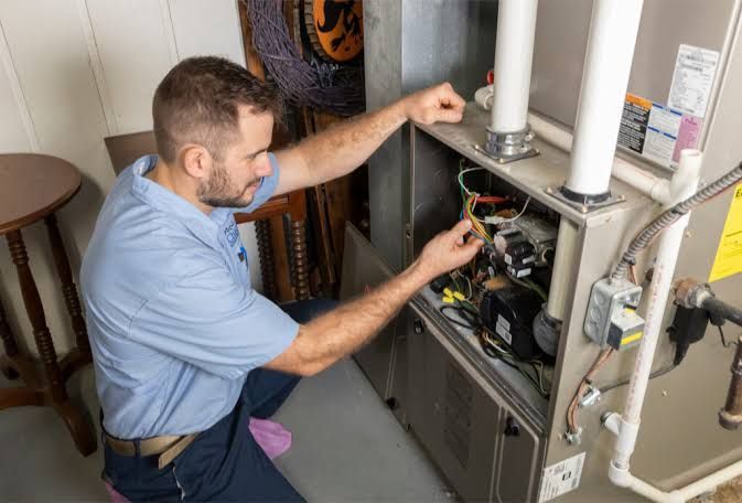 Technician inspecting an open furnace with tools in a utility room