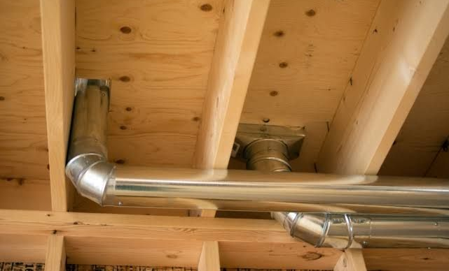 Metal HVAC ducts running through exposed wooden ceiling joists in an unfinished attic.