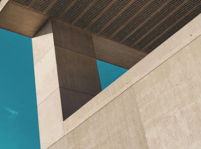 Low-angle view of a concrete architectural structure with a triangular opening against a clear blue sky.