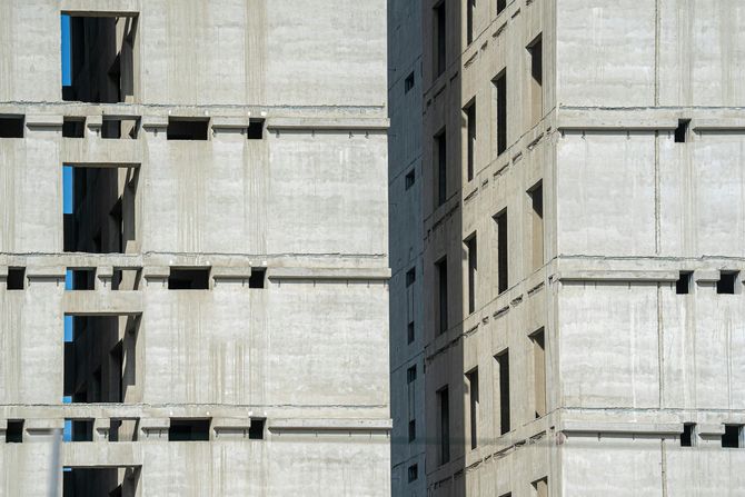 Unfinished concrete apartment building exterior featuring repetitive window openings and structural grid lines.