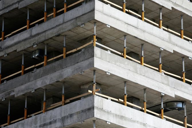 The corner of a concrete high-rise building under construction with metal support jacks and wooden safety railings.