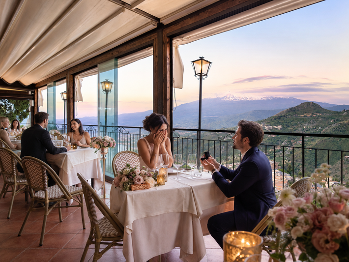 Tavoli all'aperto di un ristorante con commensali che ammirano il tramonto sulle montagne.
