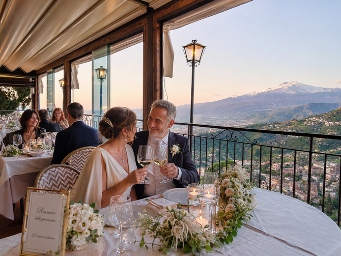 Una coppia cena su una terrazza illuminata a lume di candela con vista su una valle di montagna al tramonto.