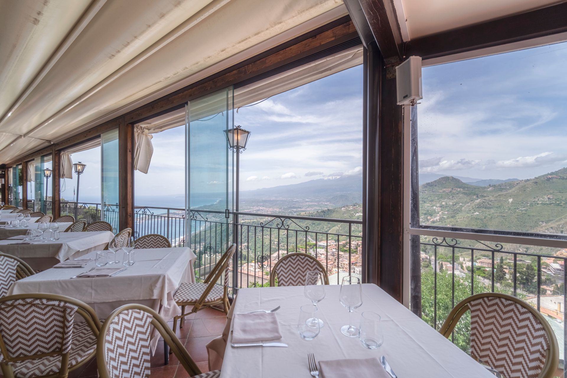 Ristorante con terrazza all'aperto, tavoli e sedie bianchi con vista sulle montagne e sul mare.