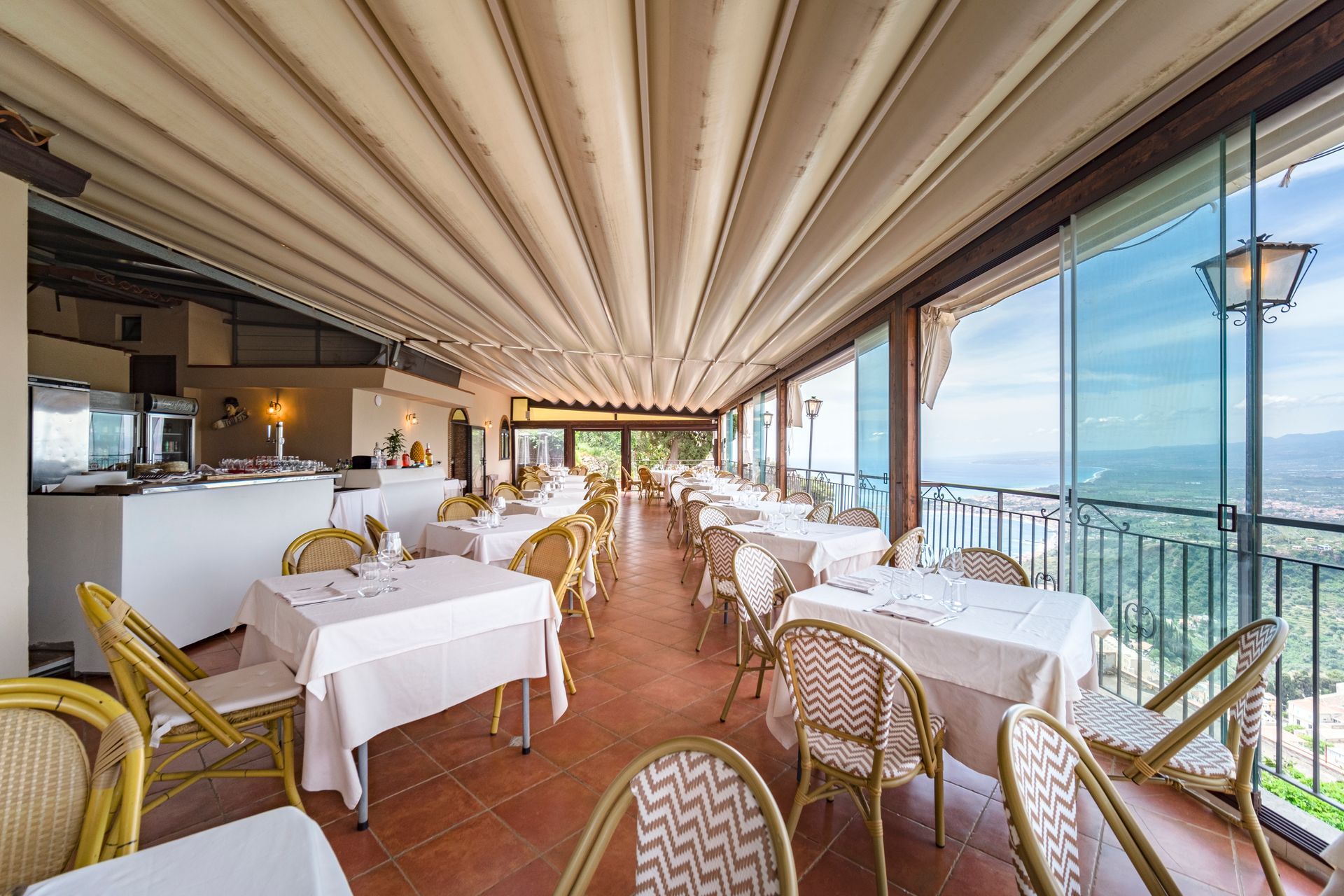 Elegante ristorante sul mare con tovaglie bianche, sedie in vimini e vista sull'oceano da una terrazza coperta.