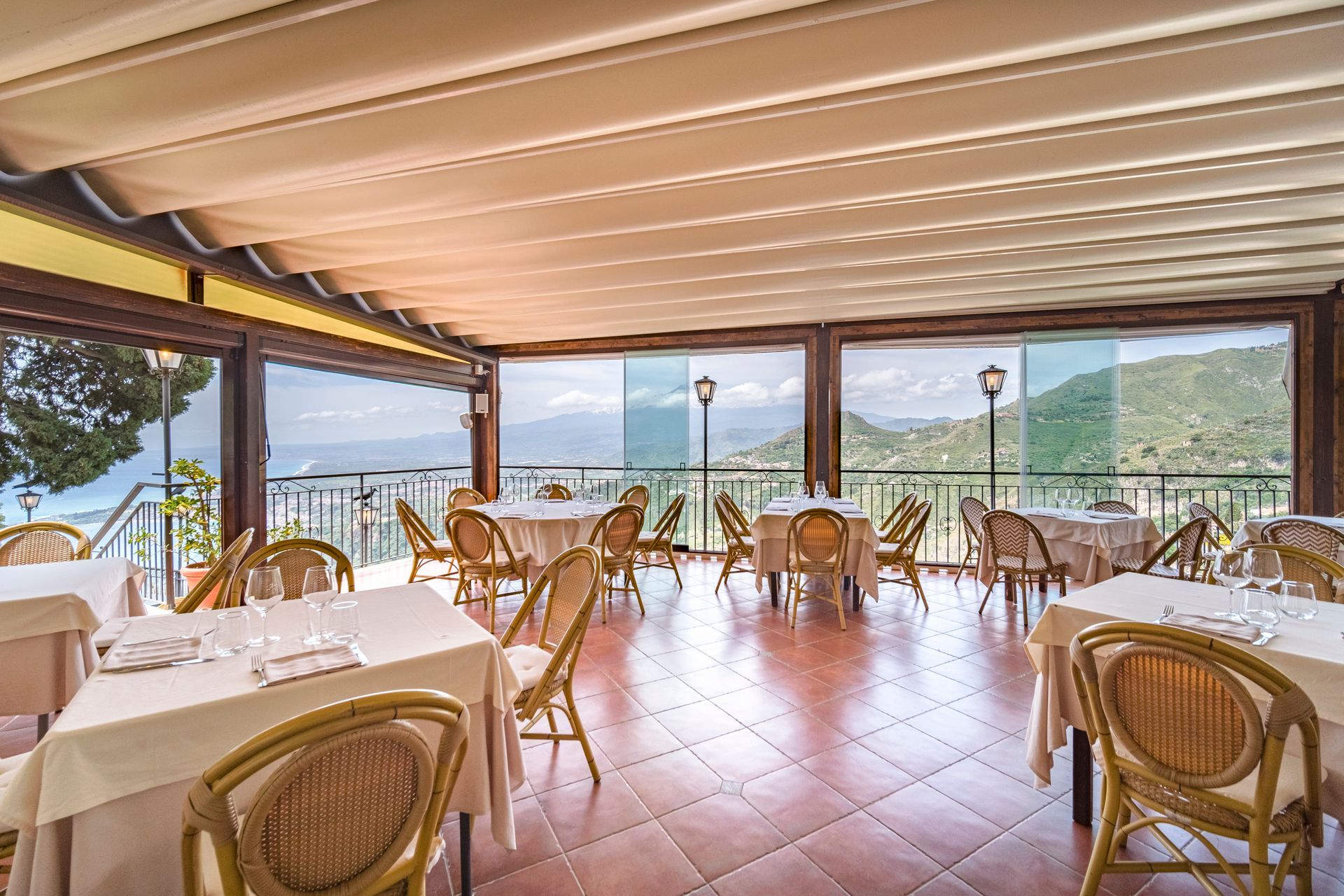 Zona pranzo all'aperto con terrazza, sedie in vimini, tovaglie bianche e vista sulle montagne.