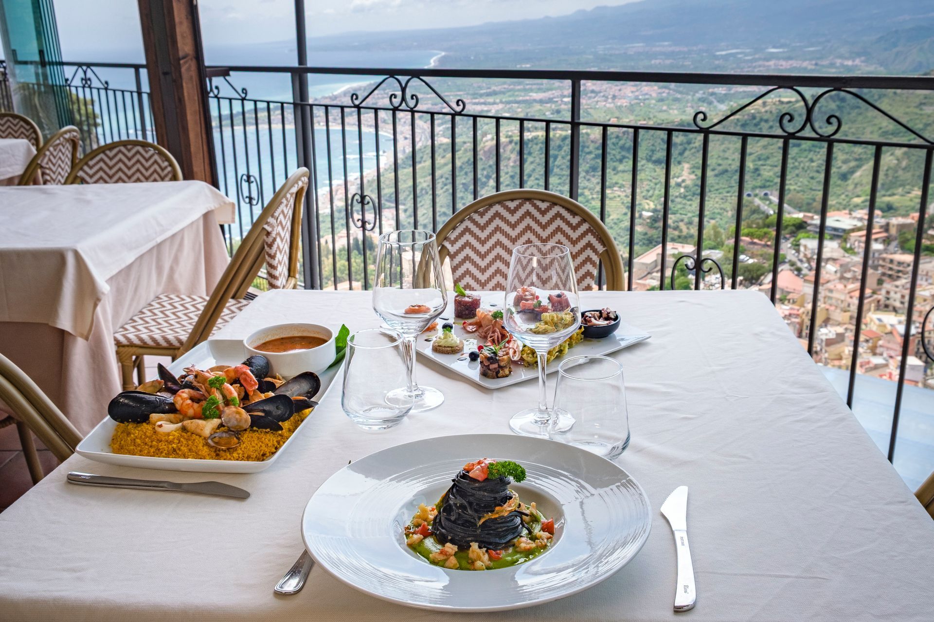 Tavolo da pranzo all'aperto con piatti serviti su una terrazza che si affaccia su una valle panoramica.