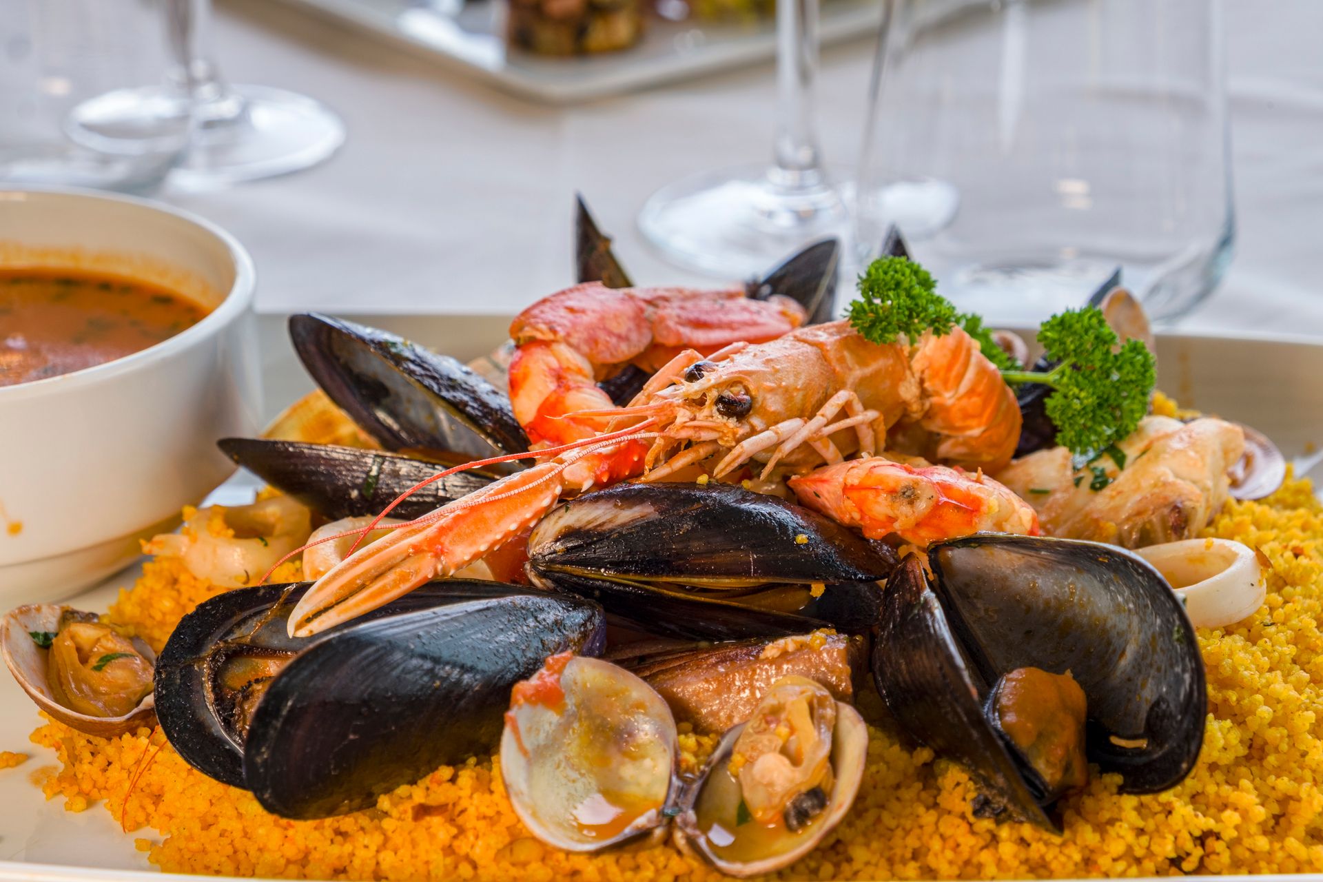 Paella di pesce con cozze, gamberi, vongole e prezzemolo, servita in un ambiente da ristorante.