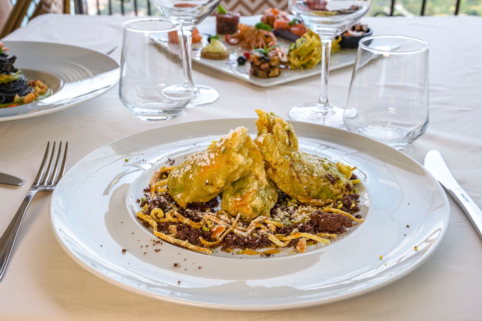 Elegante piatto gourmet impiattato con guarnizione di foglie su una tovaglia bianca in una sala da pranzo formale.