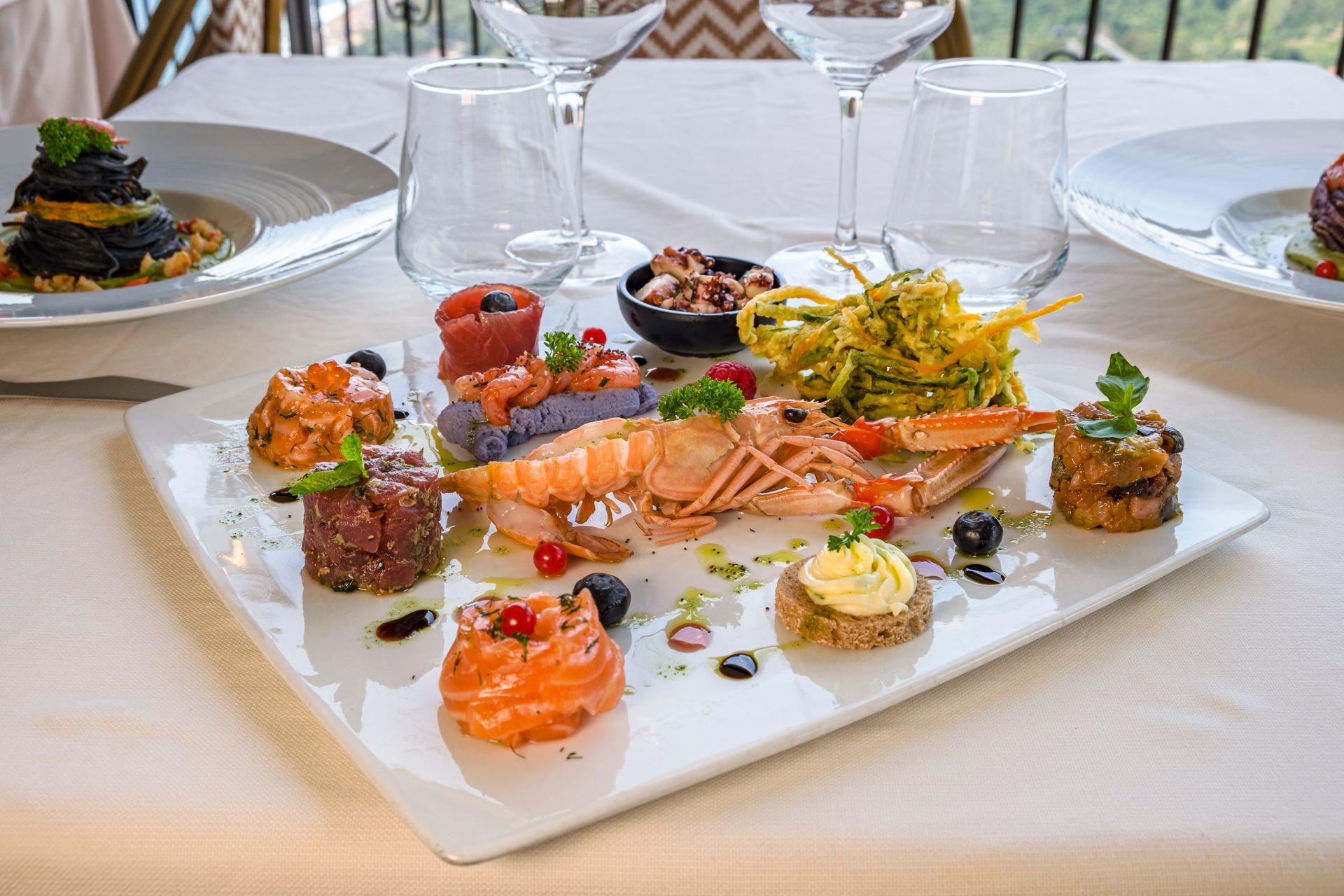 Piatto di antipasti gourmet a base di frutti di mare con salmone, gamberi e guarnizioni, servito su una tovaglia bianca.