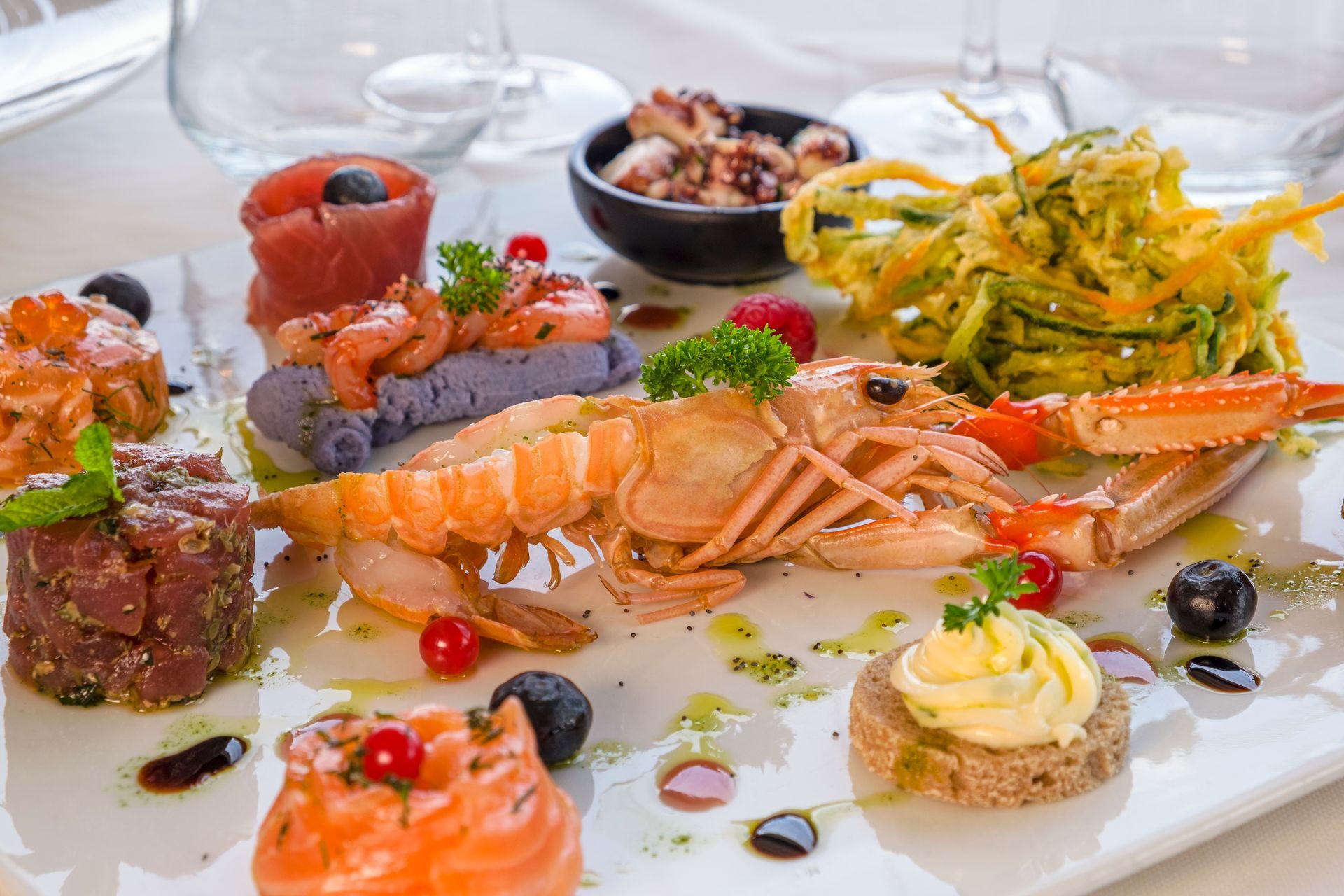 Piatto di antipasti di pesce con aragosta, sashimi, ostriche e guarnizioni su un piatto bianco.