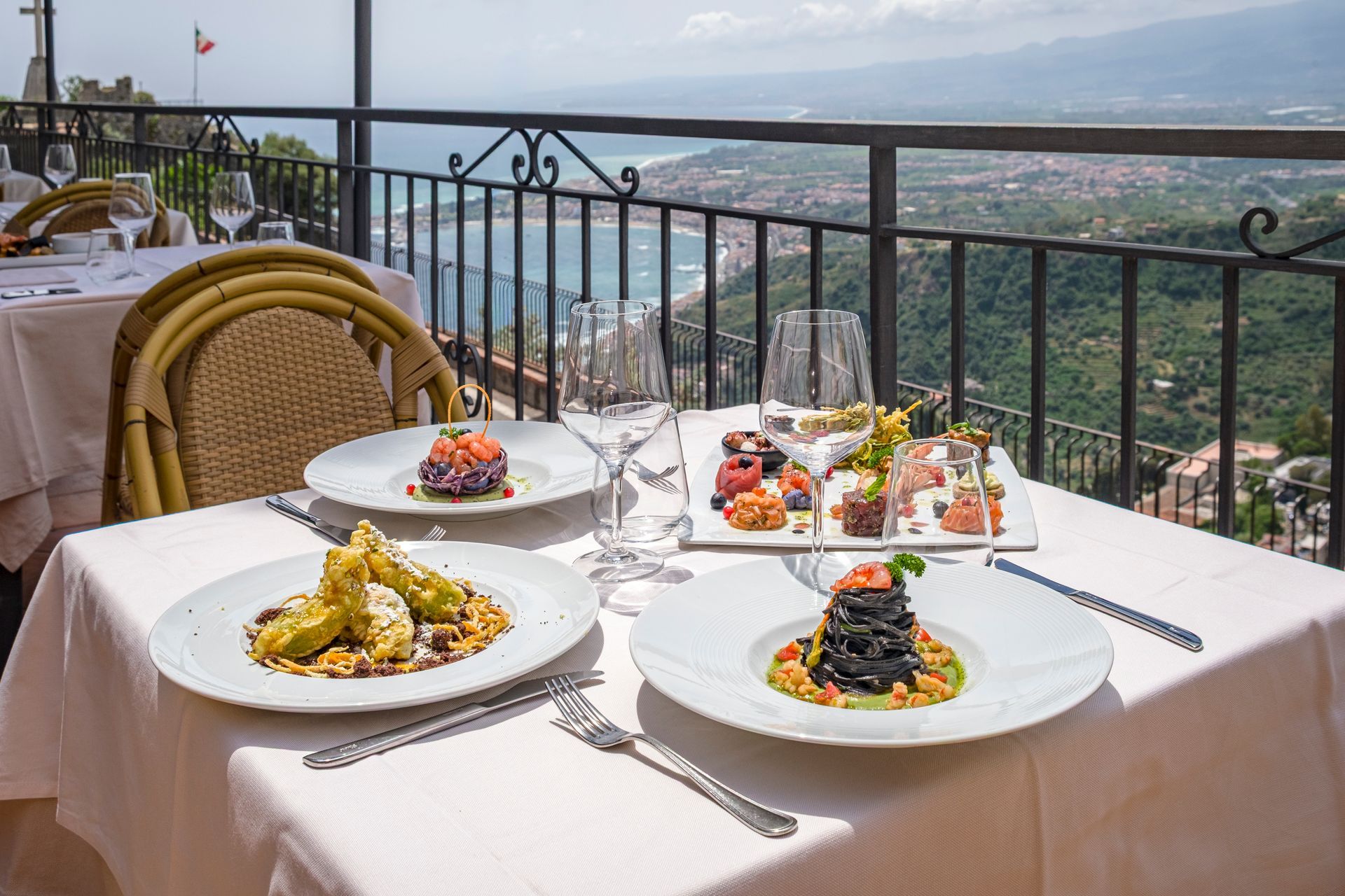 Ristorante con terrazza al tramonto, con vista sulla città, tavoli per cenare e panorama montano in lontananza.