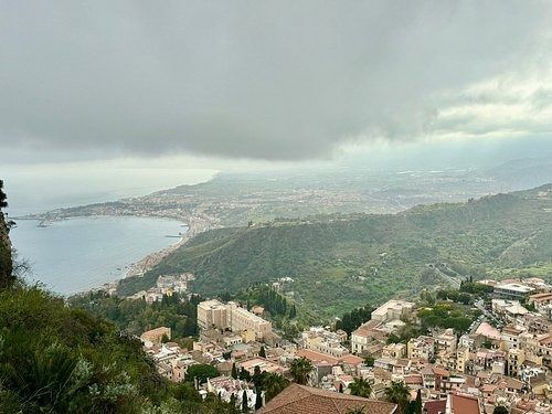 Città costiera collinare affacciata su una baia, sotto un cielo nuvoloso, con colline verdi e fitti edifici.