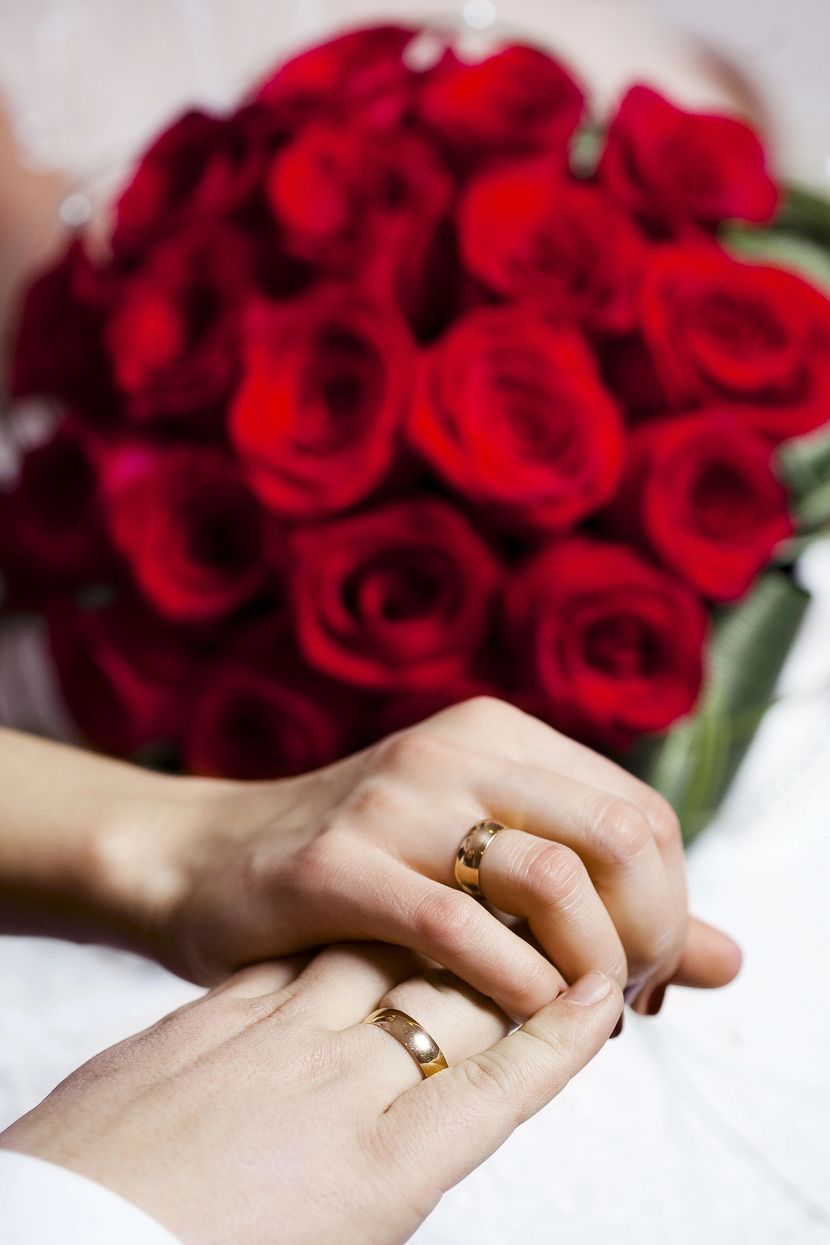 Mani con anelli d'oro posate davanti a un mazzo di rose rosse