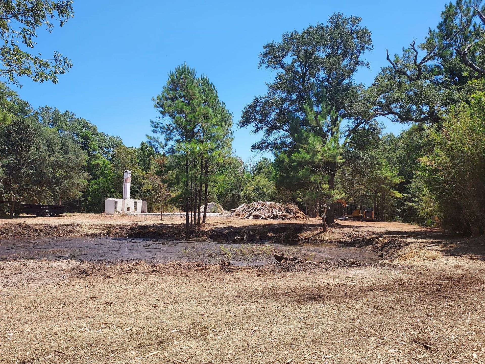 A sunny landscape featuring trees, dry grass, and a stone monument under a clear blue sky.