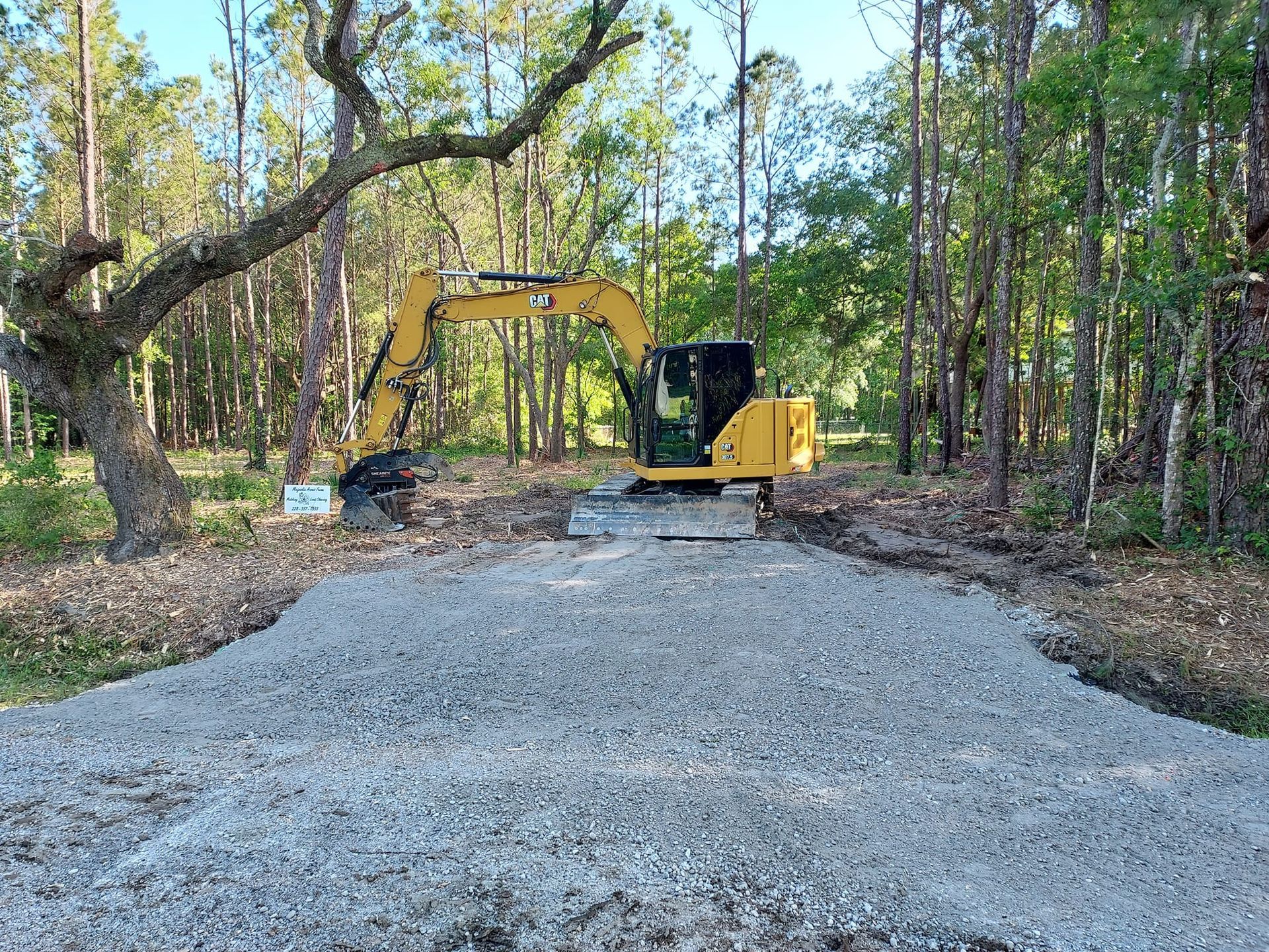 Yellow excavator on a gravel pad, near a forest.
