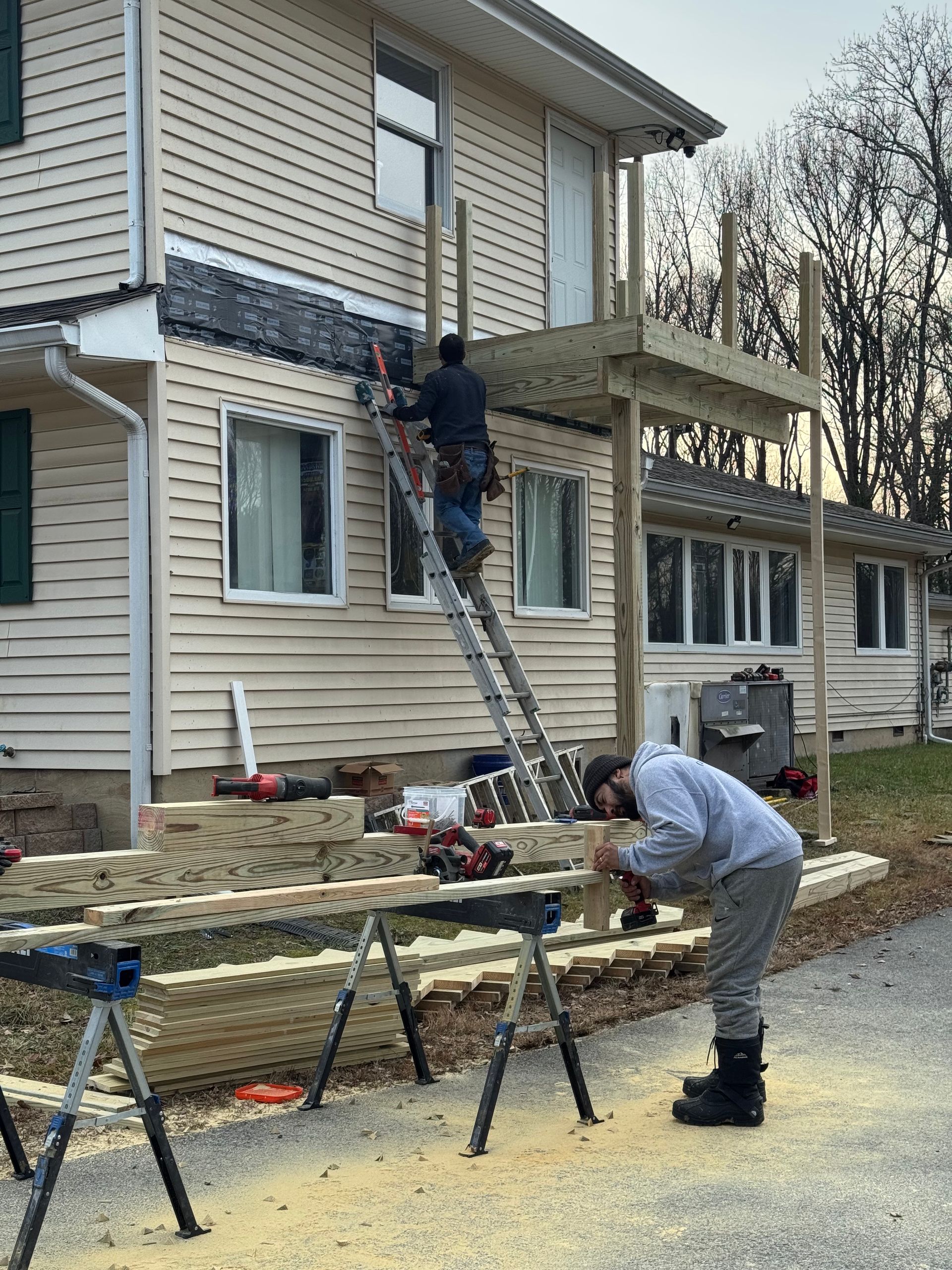 Workers on ladders repairing a house exterior, with tools and sawdust on the ground.